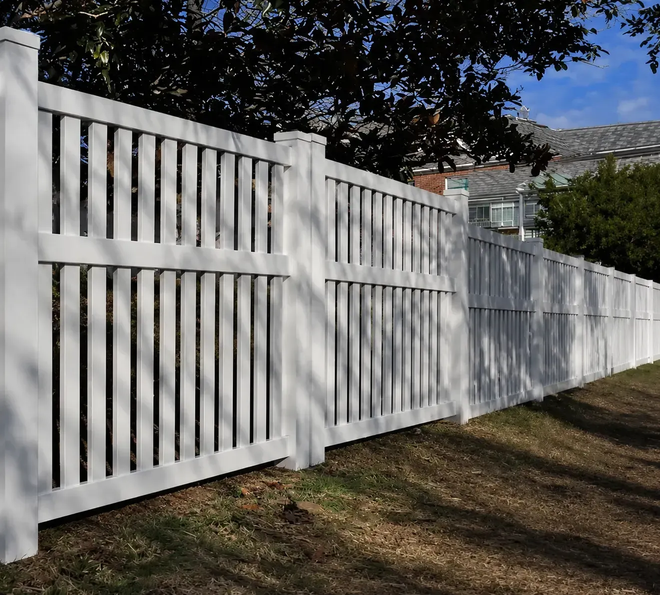 White wooden privacy fence along a grassy yard with trees and houses in the background