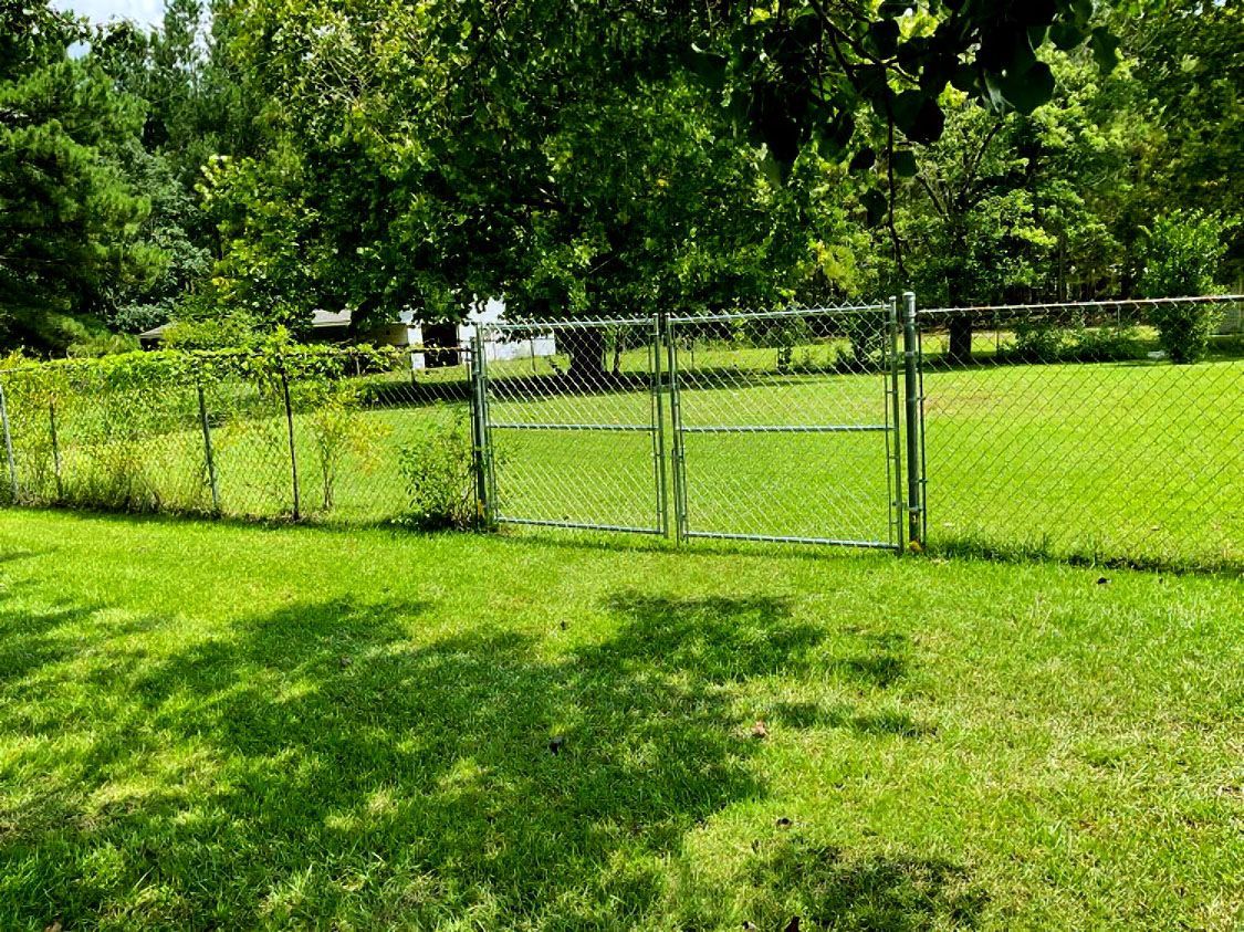 Chain-link fence beside a lush green lawn with trees in the background
