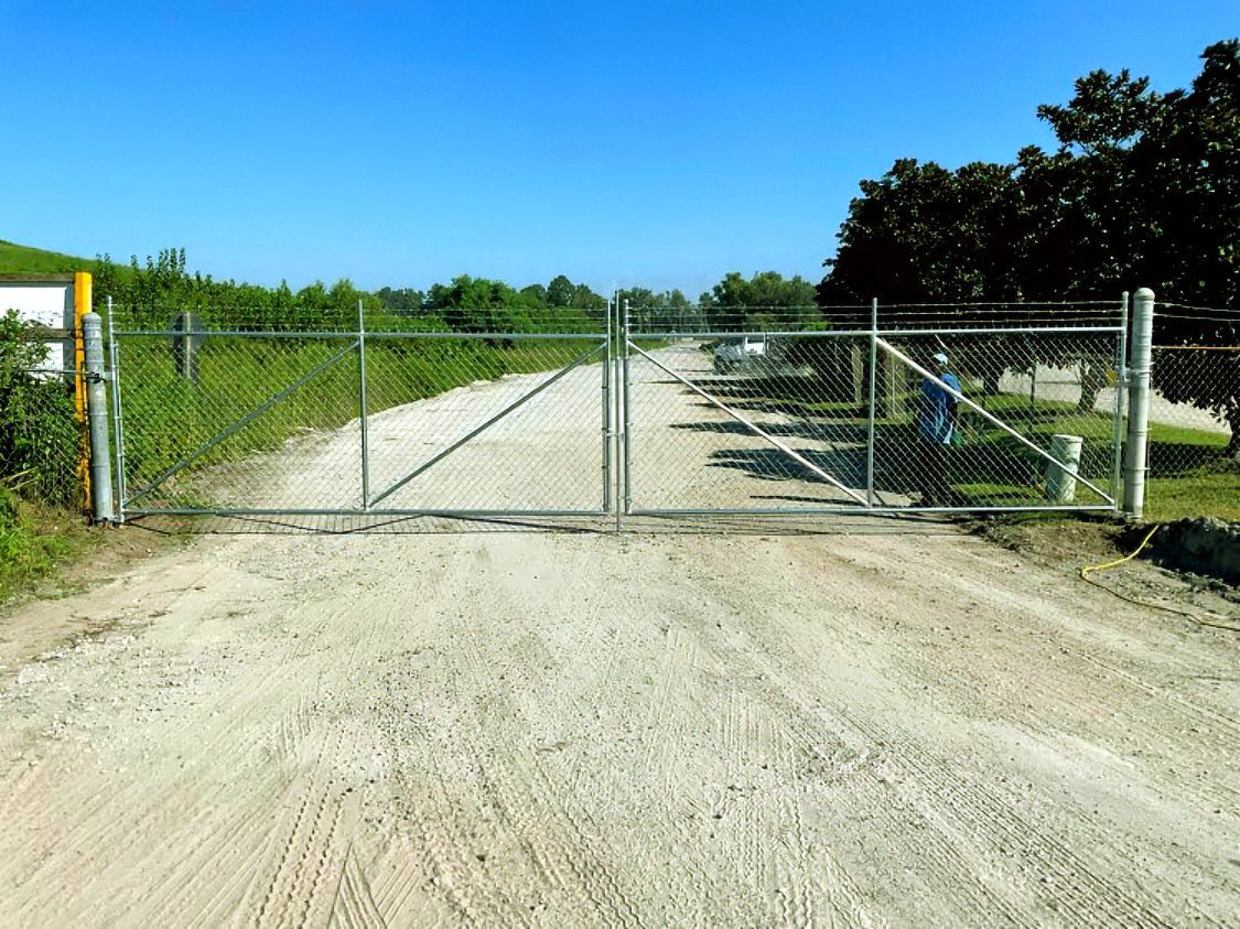Closed chain-link gate across a gravel road under a bright blue sky