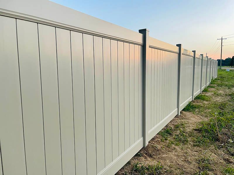White vinyl fence along a grassy roadside at sunset