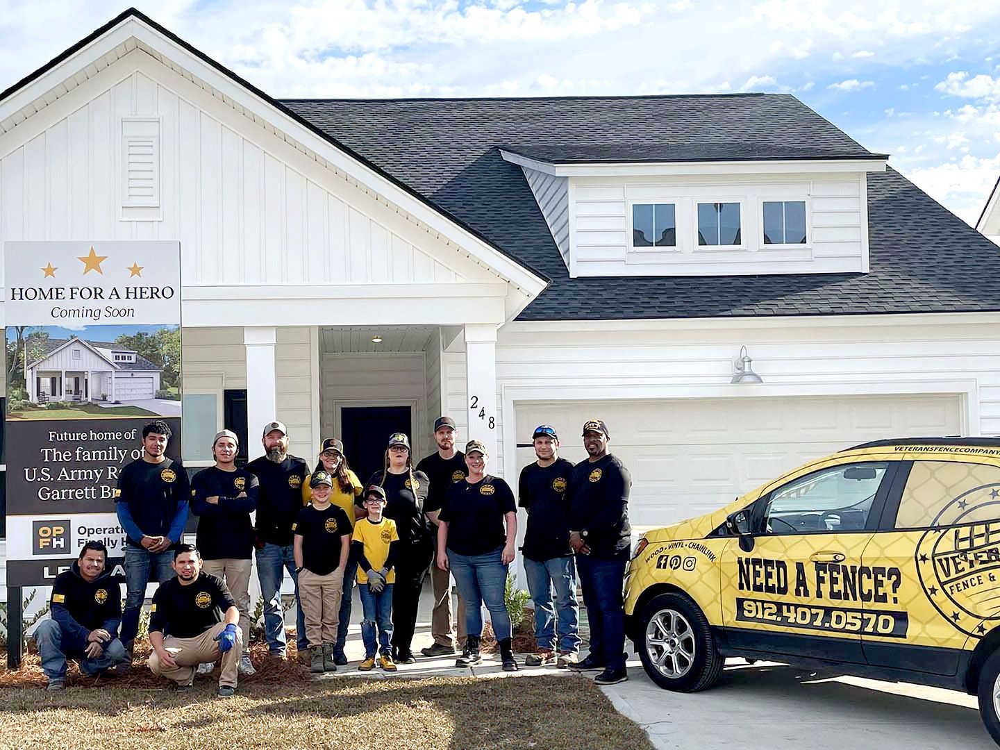 Group posing outside a white building with a branded yellow fence company car and sign.