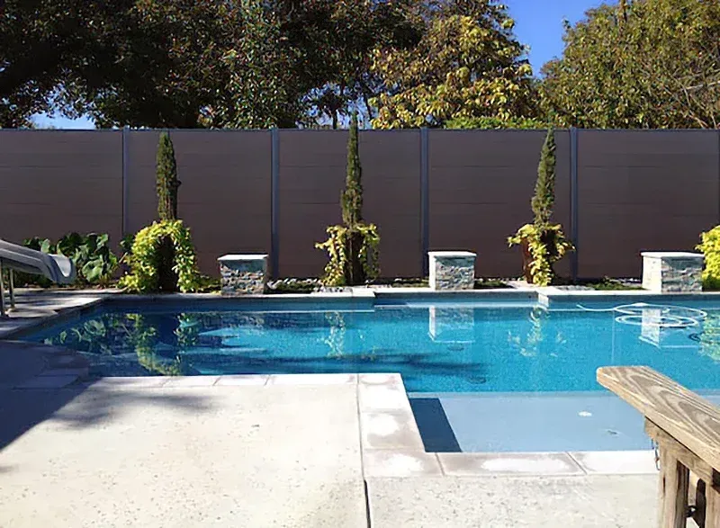 Backyard swimming pool with blue water, white patio, lounge chairs, and privacy fence.