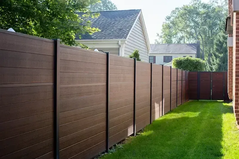 Brown wooden fence along a green lawn in a suburban backyard with houses in the background