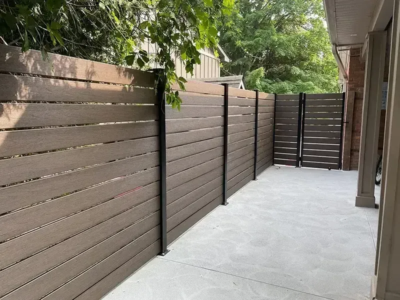 Narrow concrete patio with brown horizontal fence panels and trees overhead