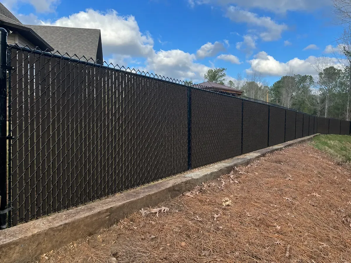 Black chain-link fence along a dirt path under a blue sky with clouds