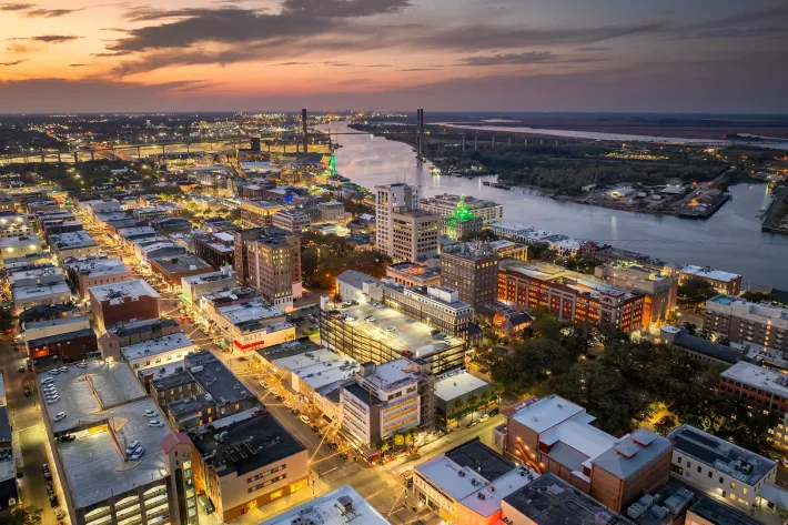 Aerial city skyline at sunset with lit buildings, streets, and a river curving through the background