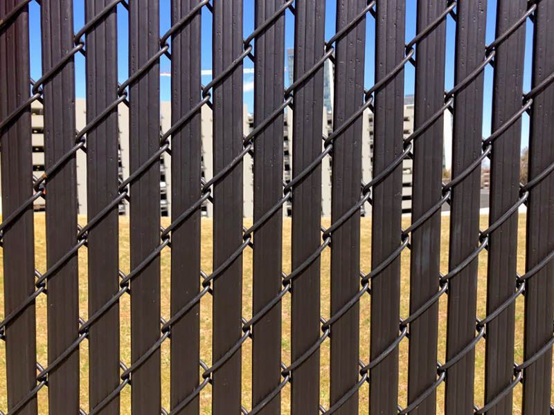 Black metal fence with vertical bars and diamond mesh against a blue sky and tan wall.