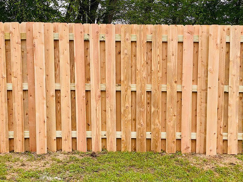 Wooden privacy fence with vertical slats above a patch of grass and dirt.