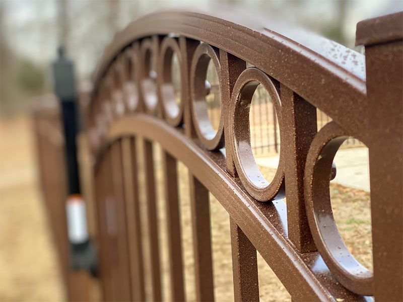 Brown metal garden bridge railing with circular cutouts in a blurred outdoor setting