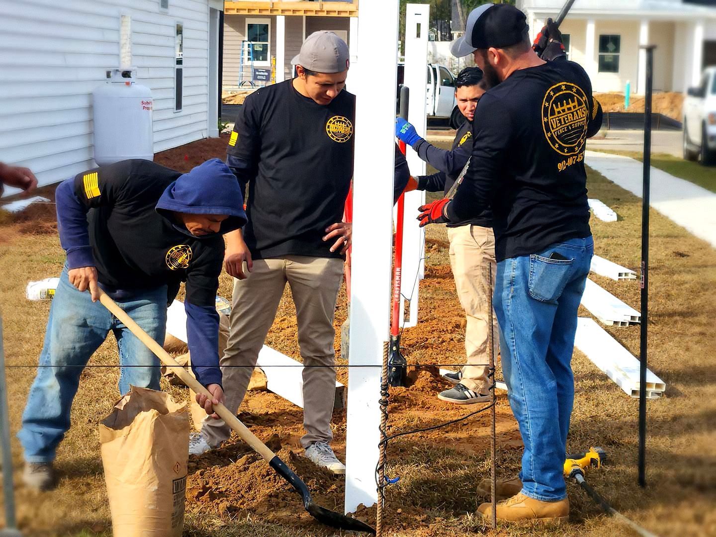 Volunteers shoveling mulch around a white post in a residential yard on a sunny day