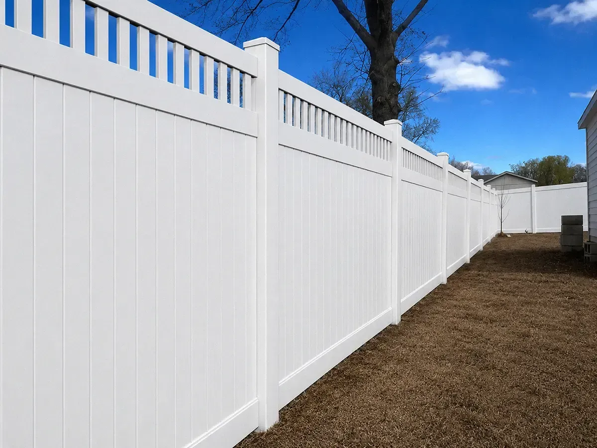 Long white vinyl privacy fence along a yard under a blue sky