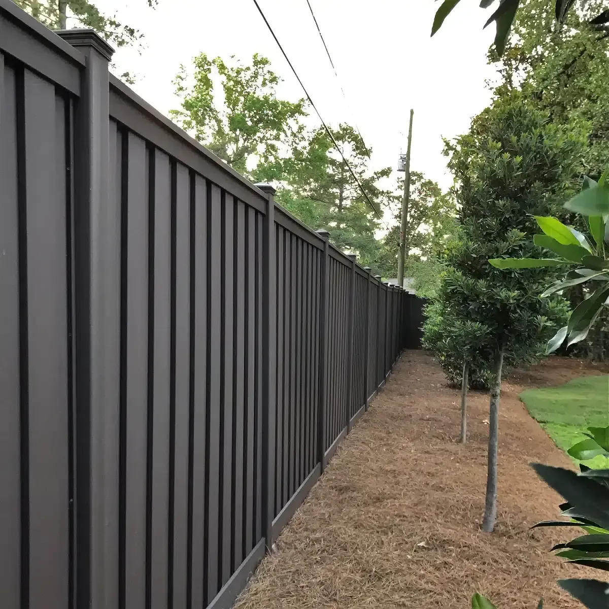 Long dark metal fence beside a narrow dirt path and trees in a green yard