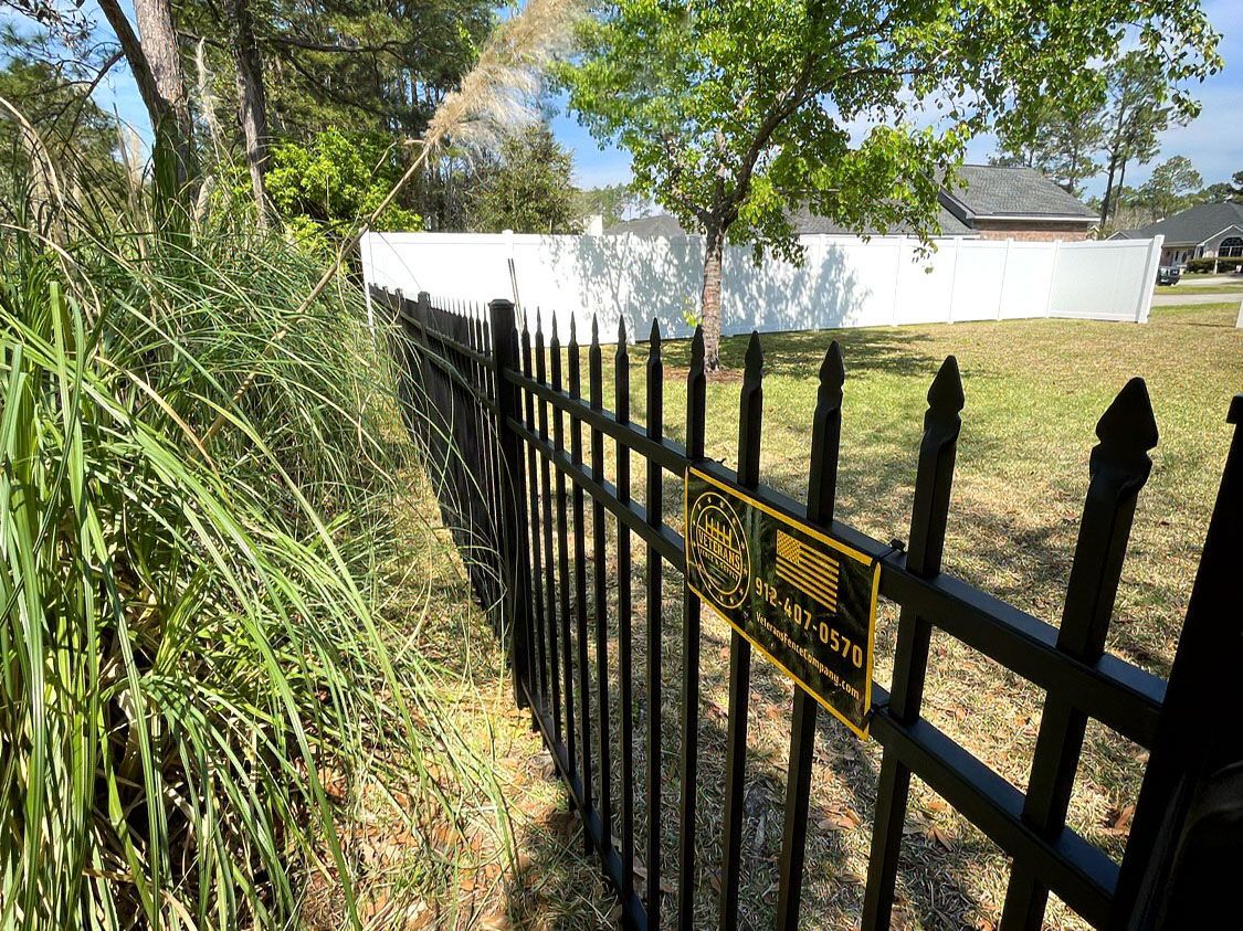 Black metal fence beside tall grass and trees in a sunny yard