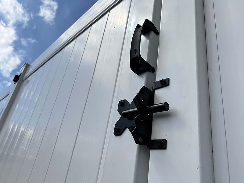 Black metal door hinges on a white corrugated metal wall under a blue sky.
