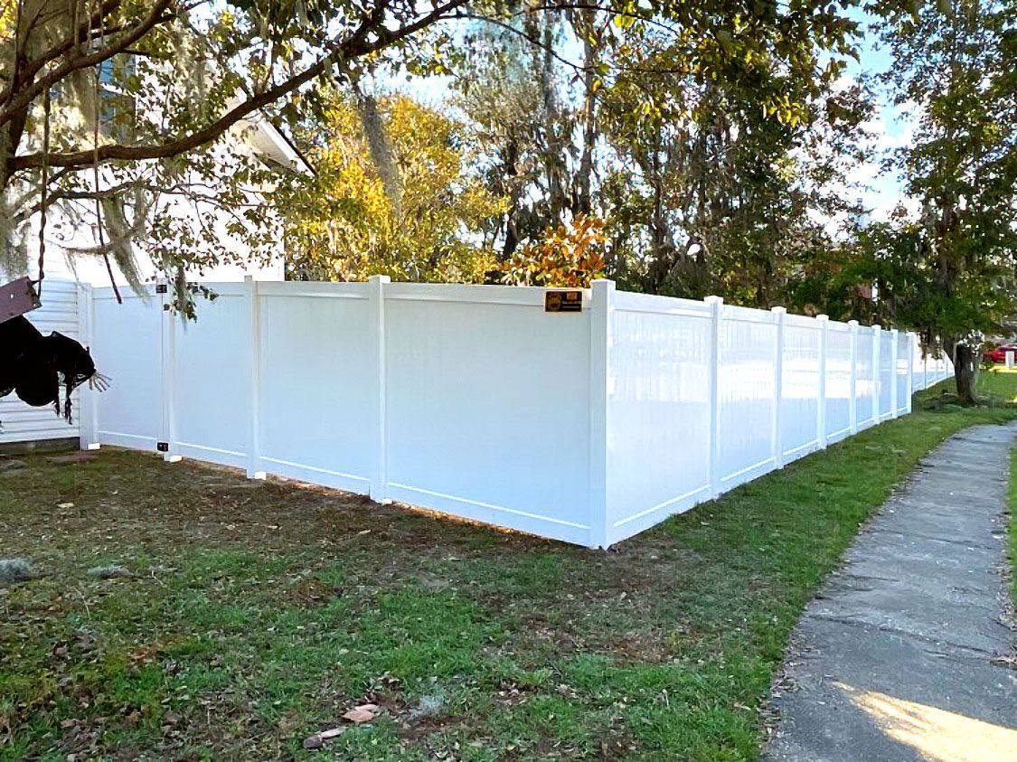 White vinyl fence along a grassy sidewalk under trees on a sunny day