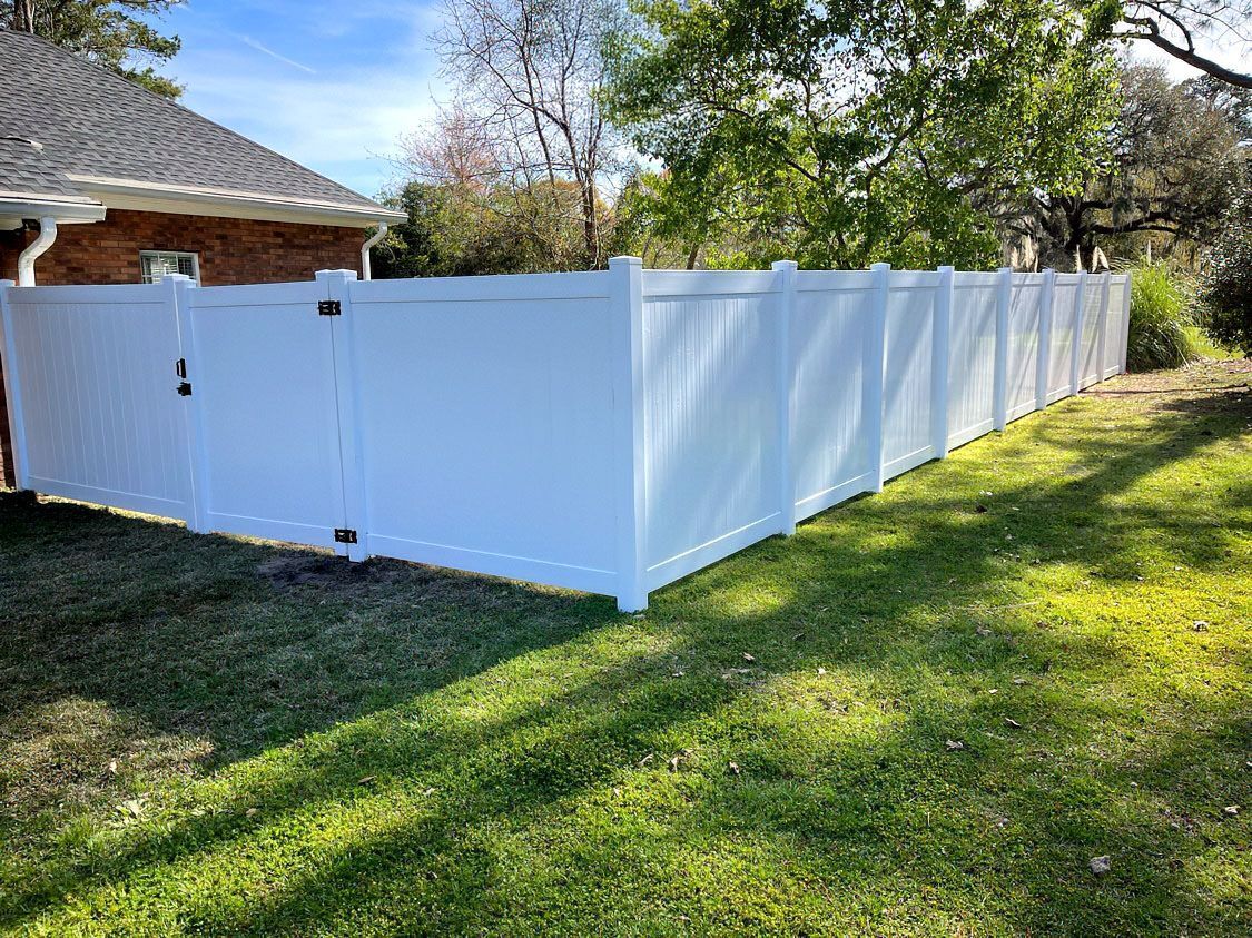White vinyl privacy fence enclosing a backyard beside a house on a sunny lawn