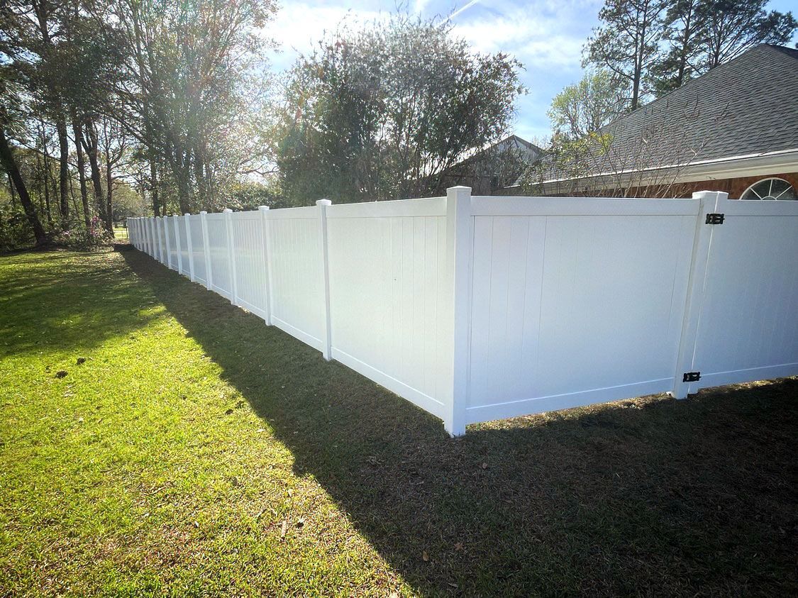 White vinyl fence enclosing a grassy backyard beside a house, with trees in the background