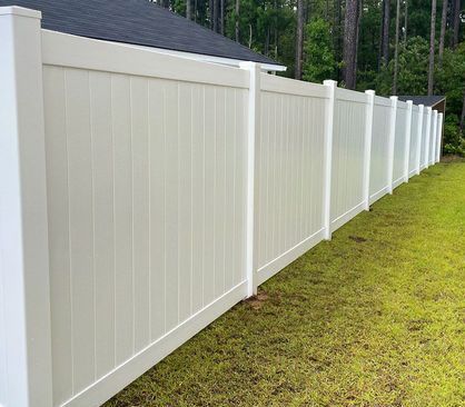 White vinyl privacy fence along a grassy yard beside a house and wooded area