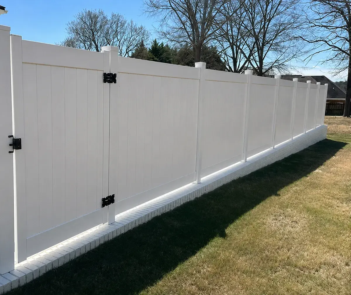 White vinyl privacy fence along a grassy yard under a clear blue sky