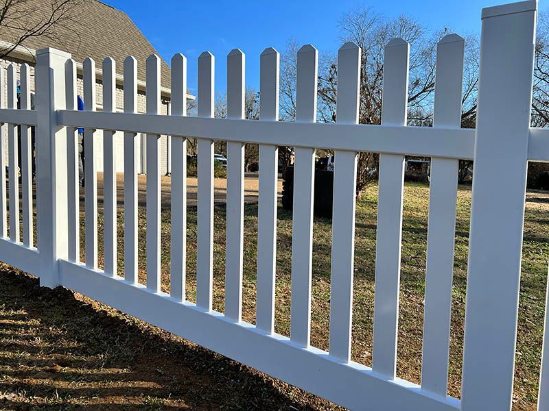 White wooden picket fence beside a grassy yard under a clear blue sky