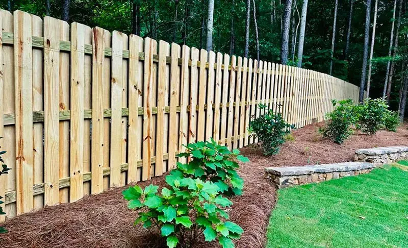 Wooden privacy fence along a landscaped garden bed with shrubs and green lawn