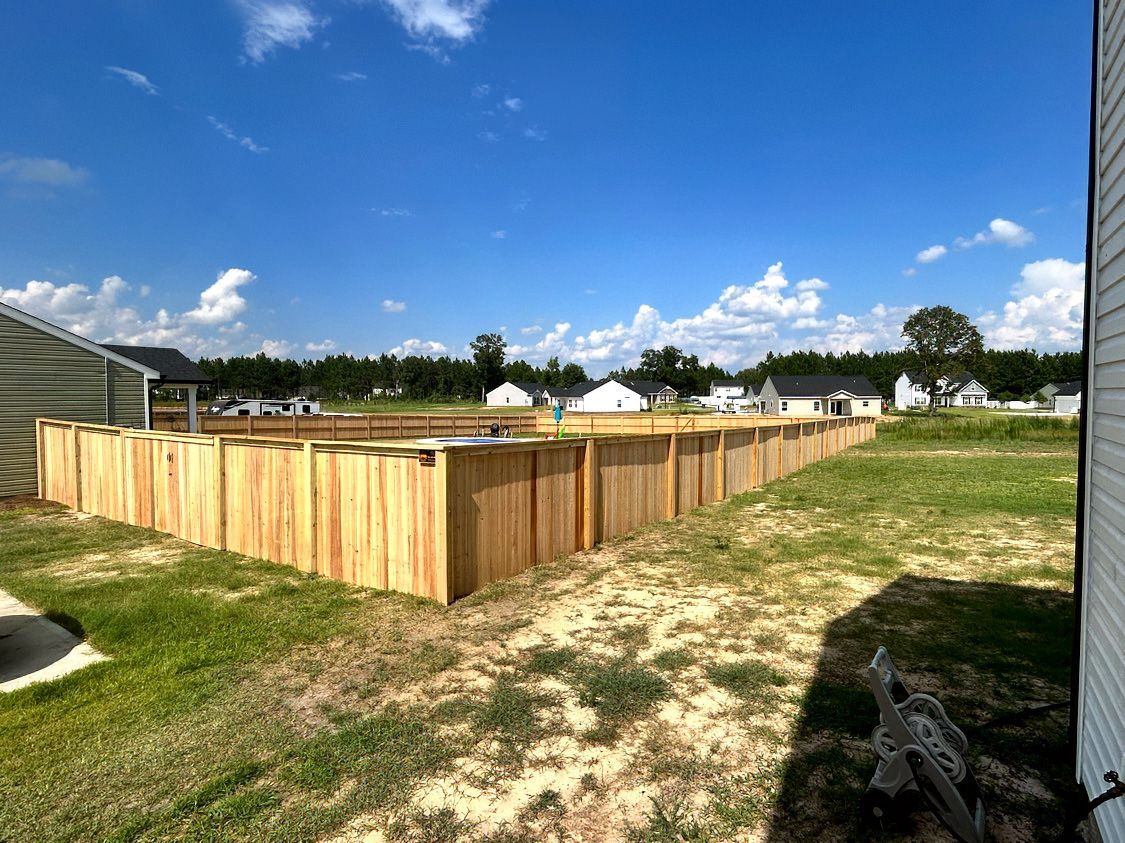 Wooden fenced enclosure in a grassy field under a blue sky with clouds