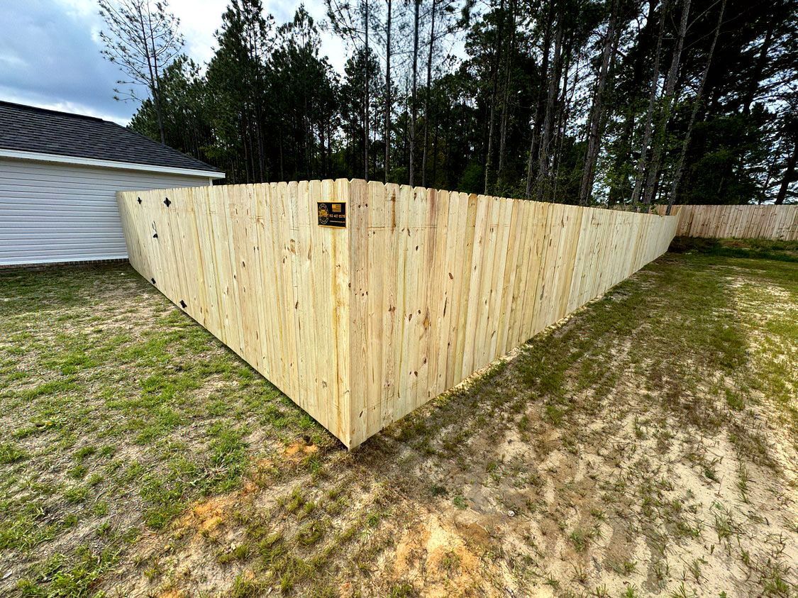Wooden privacy fence enclosing a yard beside a white house and tree line