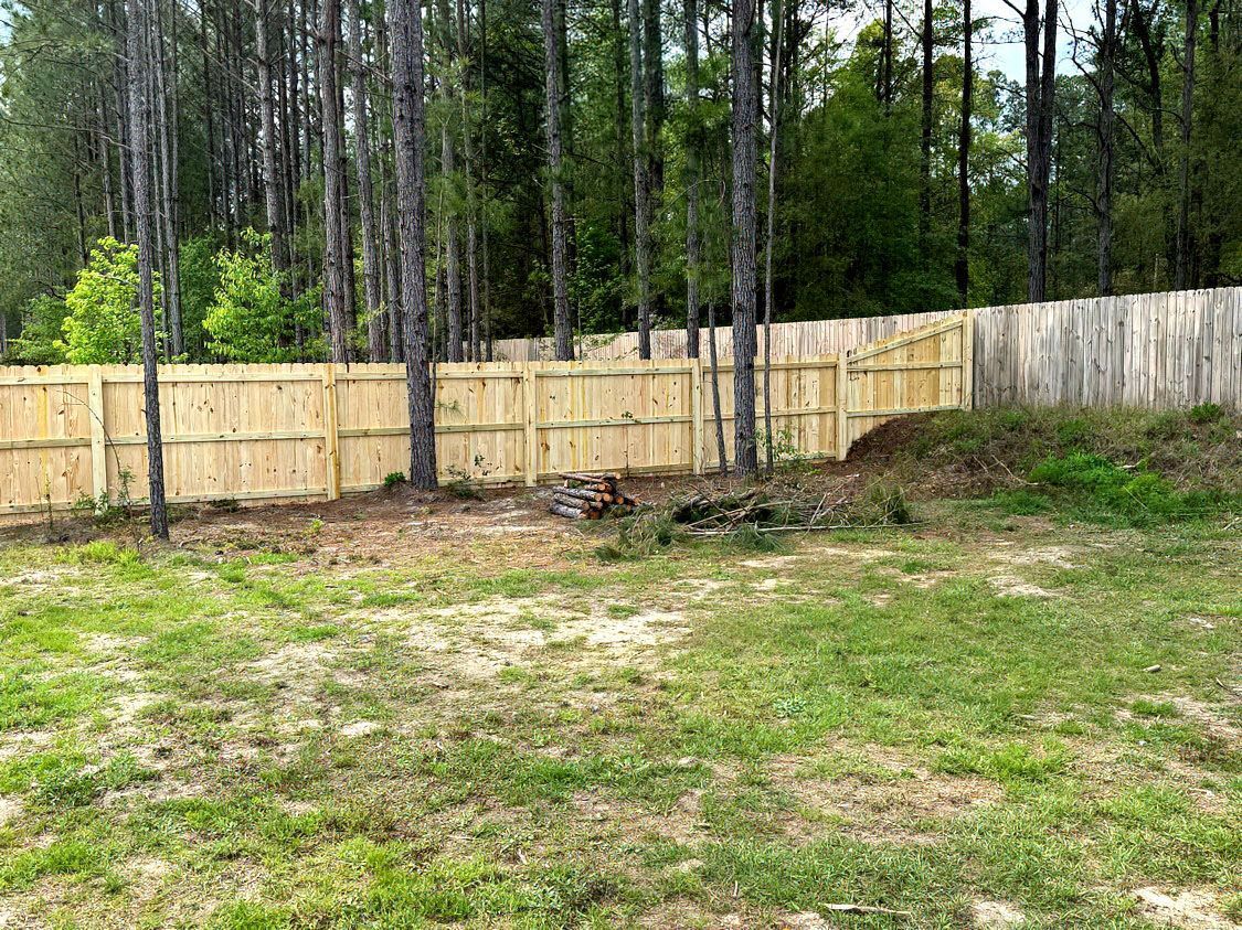 Backyard with new wooden fence, grassy yard, and tall trees in the background