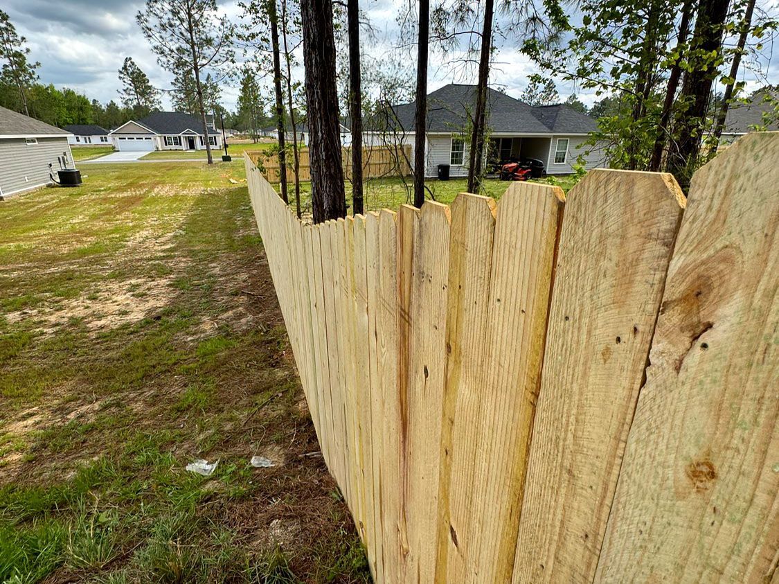 Close-up of a weathered wooden fence beside a grassy yard and houses in the background.