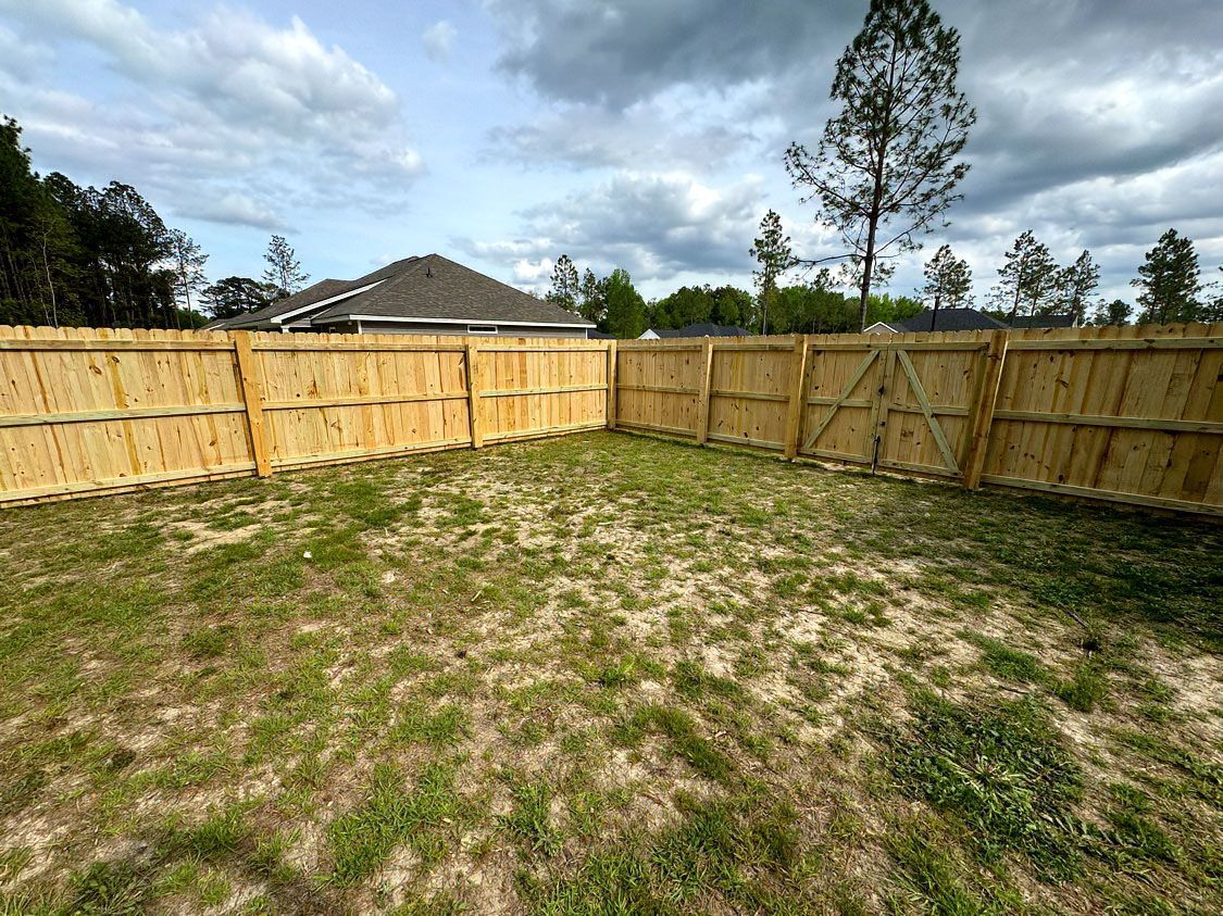 Grassy backyard with a wooden privacy fence and cloudy sky overhead