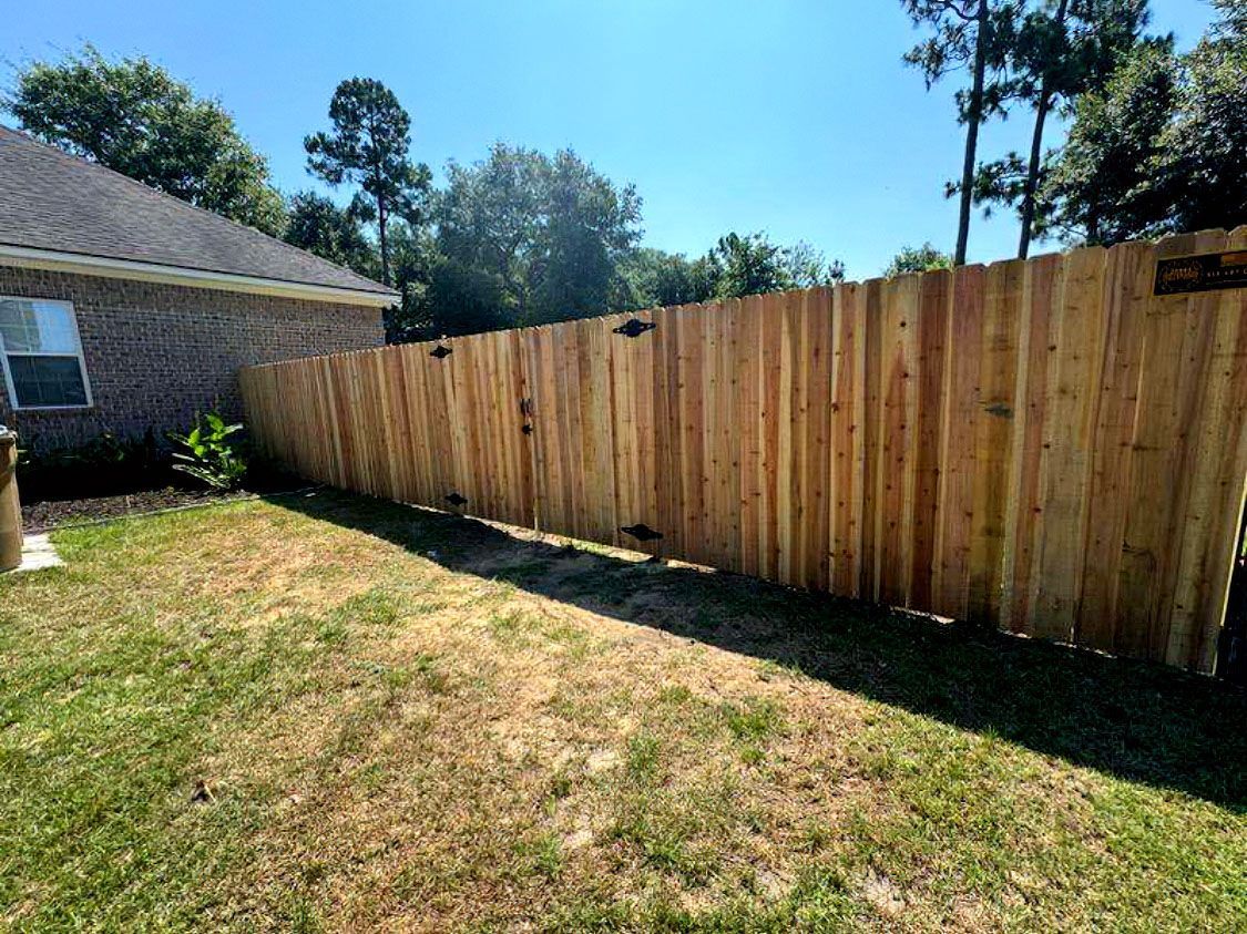 Wooden privacy fence beside a house in a sunny backyard with patchy grass