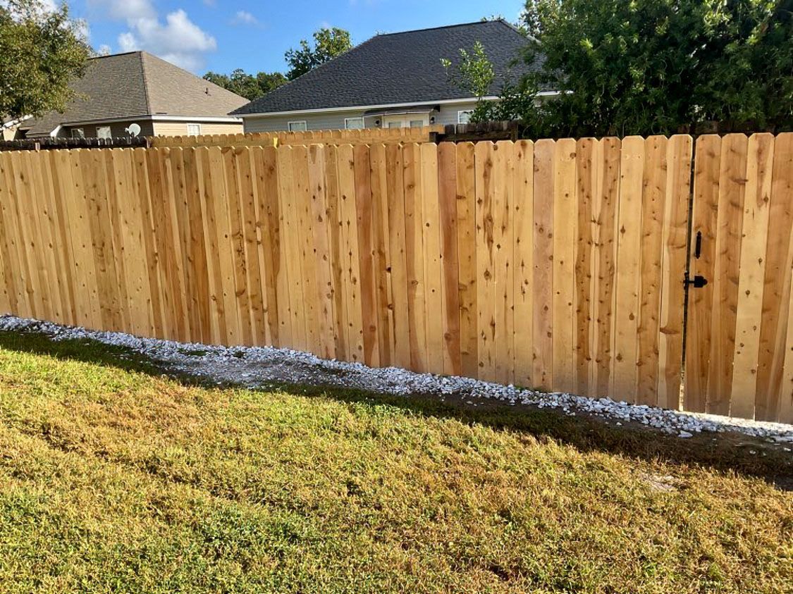 New wooden privacy fence along a grassy yard with houses and trees behind it