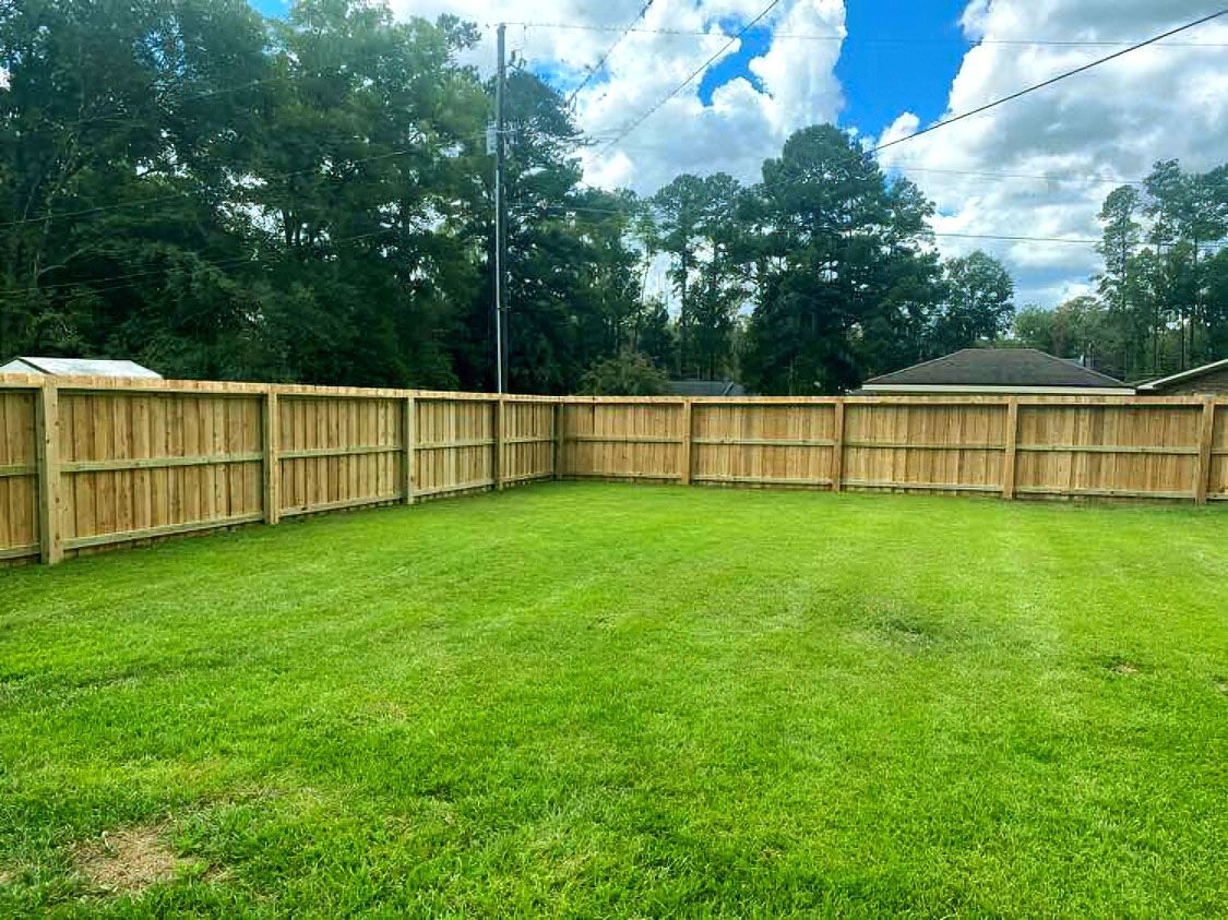 Spacious green backyard with a wooden privacy fence and trees under a partly cloudy sky