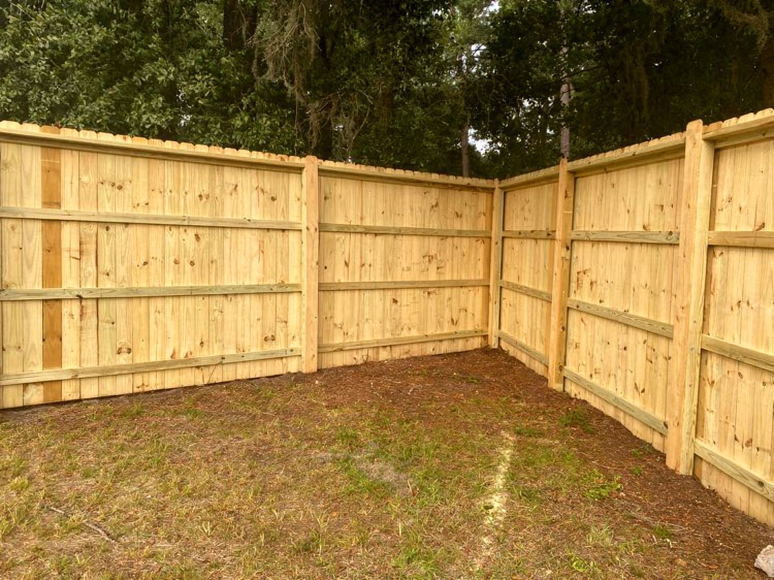 New wooden privacy fence enclosing a bare dirt yard in a corner lot