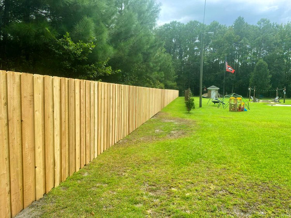 Wooden fence bordering a grassy park with playground equipment and trees in the background
