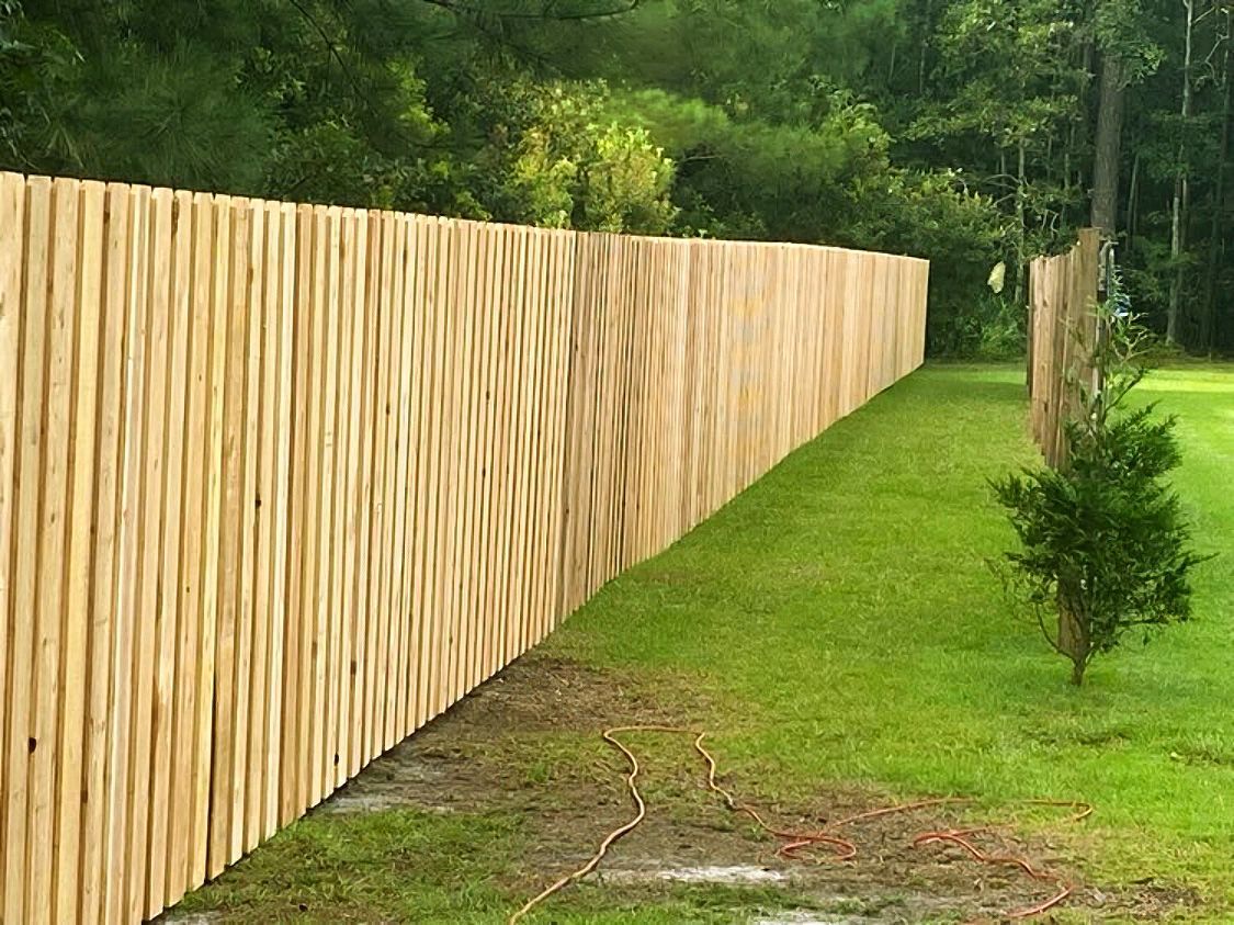 Wooden privacy fence along a grassy yard beside trees and a narrow path