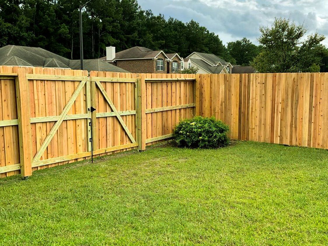 Backyard with a wooden fence, green lawn, and a small shrub under a cloudy sky