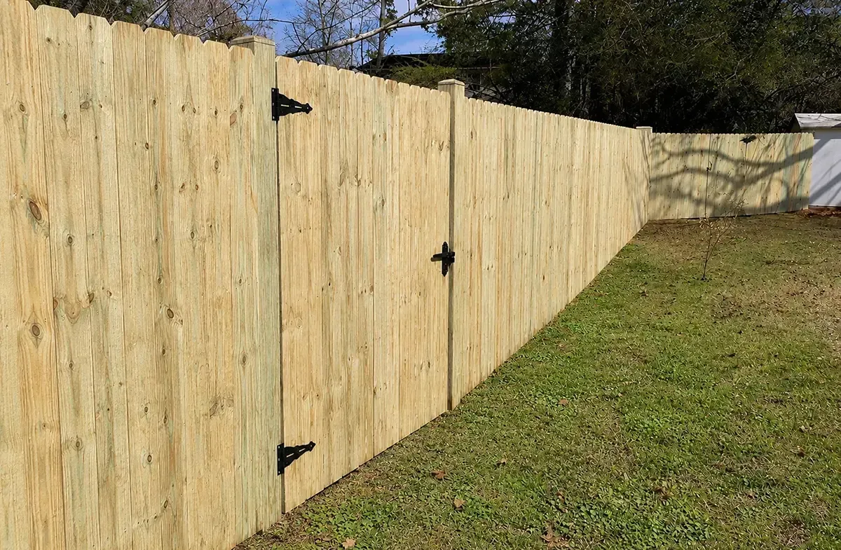Long wooden fence with black gate latches along a grassy yard