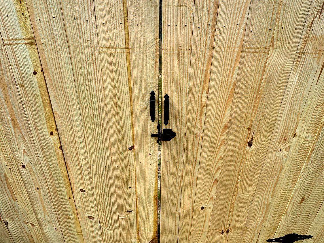 Close-up of a light wooden gate with a black metal latch centered on it