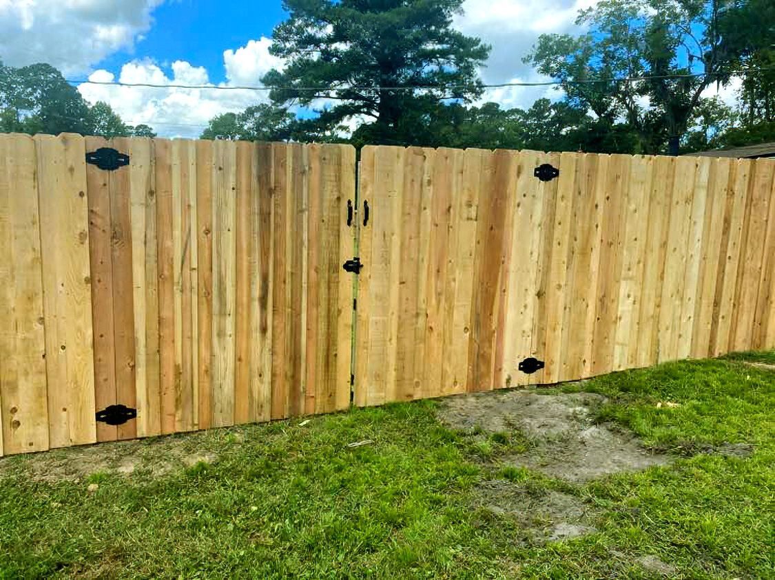 Wooden fence with black hinges across a grassy yard under a partly cloudy sky