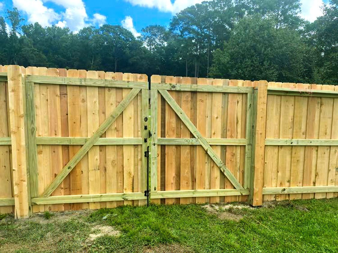 Wooden backyard fence with a double gate and trees behind it under a blue sky