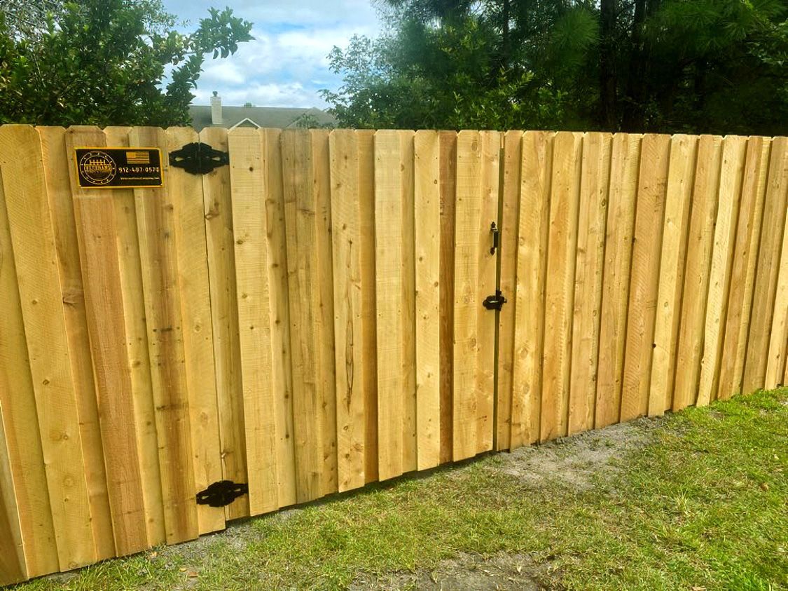 Wooden privacy fence with a gate beside a grassy yard and trees in the background