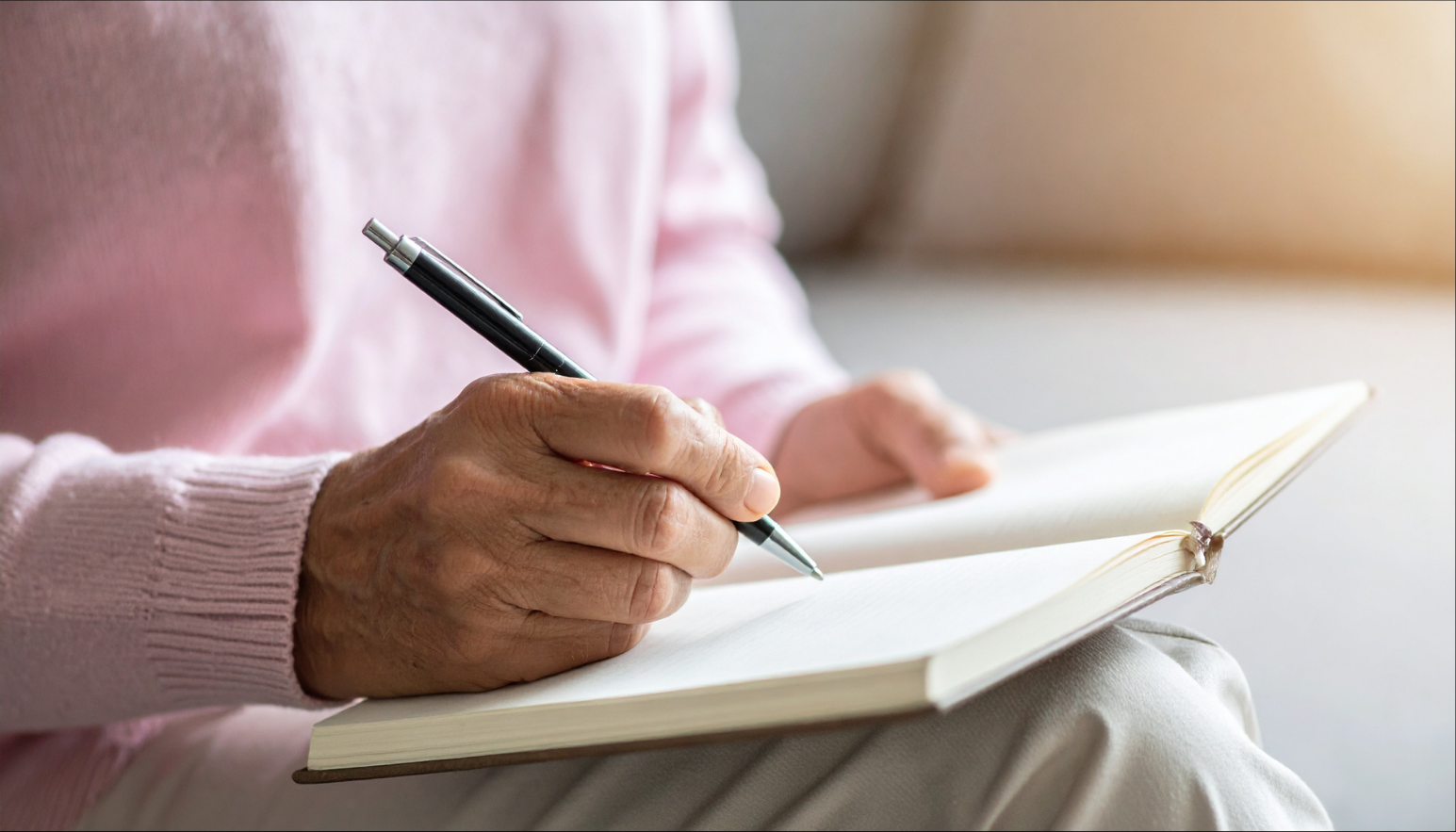 A close-up of a person in a pink sweater writing in a notebook, building a bone health plan.