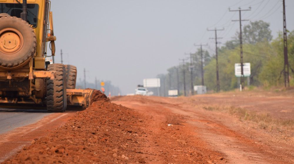 An Earthmoving Bulldozer Is Driving Down A Dirt Road — Coleman's Contracting & Earthmoving In Katherine, NT