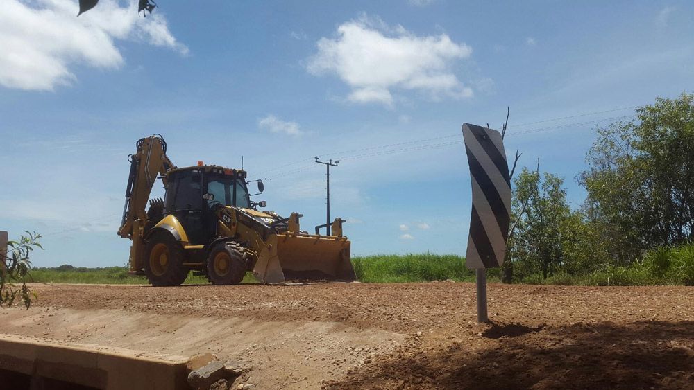 A Bulldozer Is Driving Down A Dirt Road Next To A Sign — Coleman's Contracting & Earthmoving In Katherine, NT