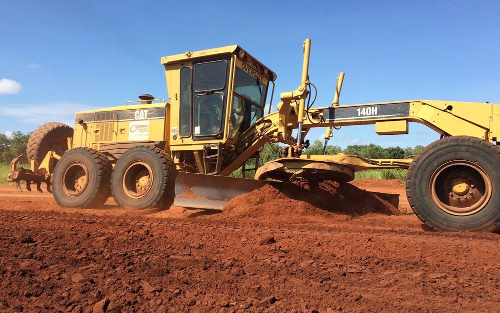 A Yellow Caterpillar Grader Is Moving Dirt In A Field — Coleman's Contracting & Earthmoving In Humpty Doo, NT