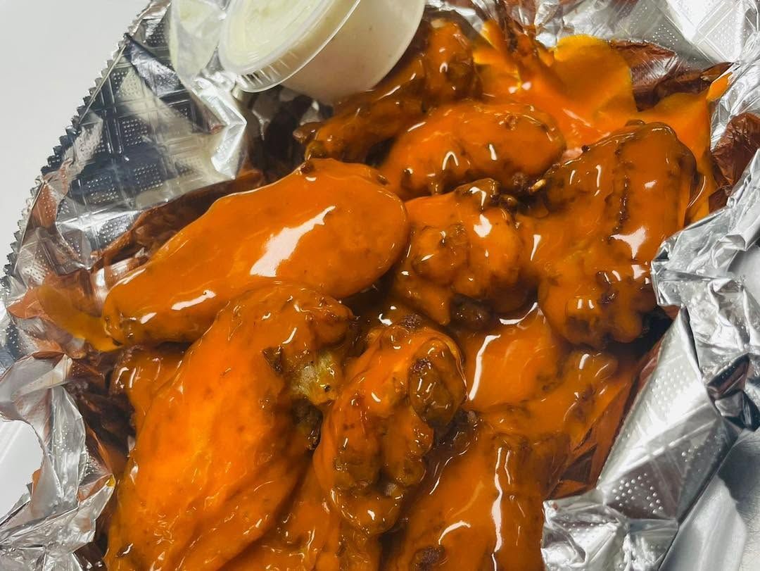 Buffalo chicken wings on foil with a small cup of dipping sauce