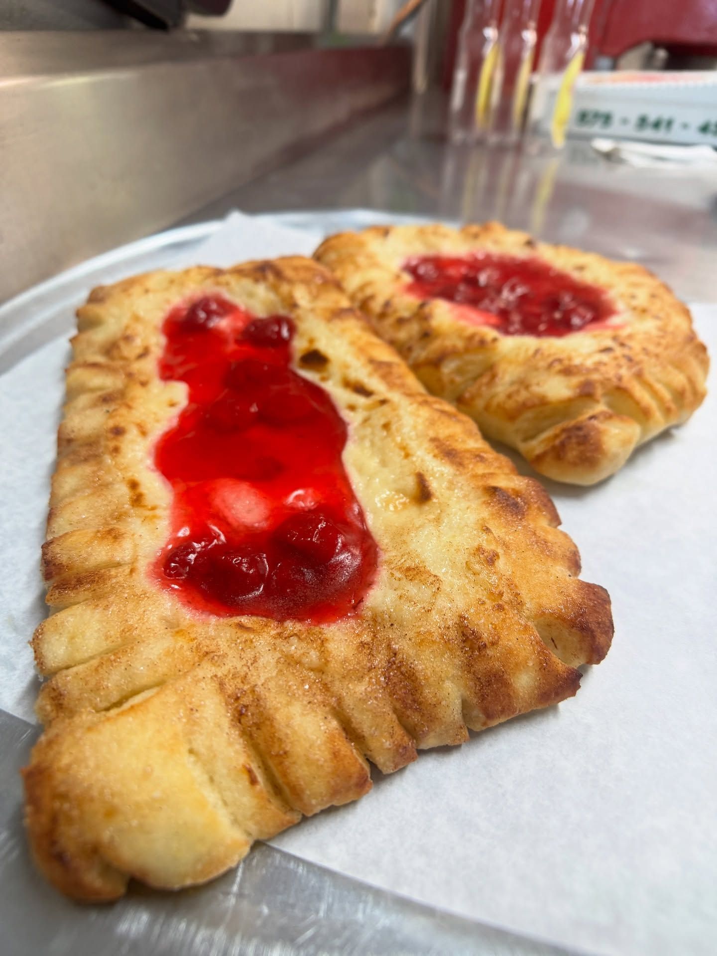 Two baked turnovers with red fruit filling on parchment paper