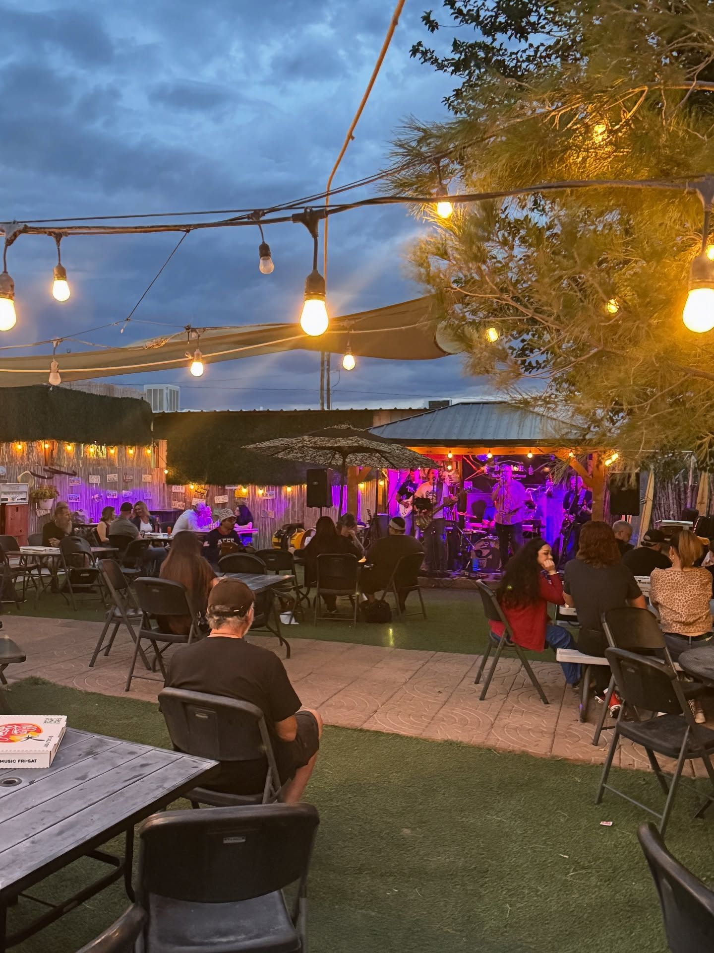 Outdoor evening event with string lights, purple-lit seating area, and guests gathered on a patio.