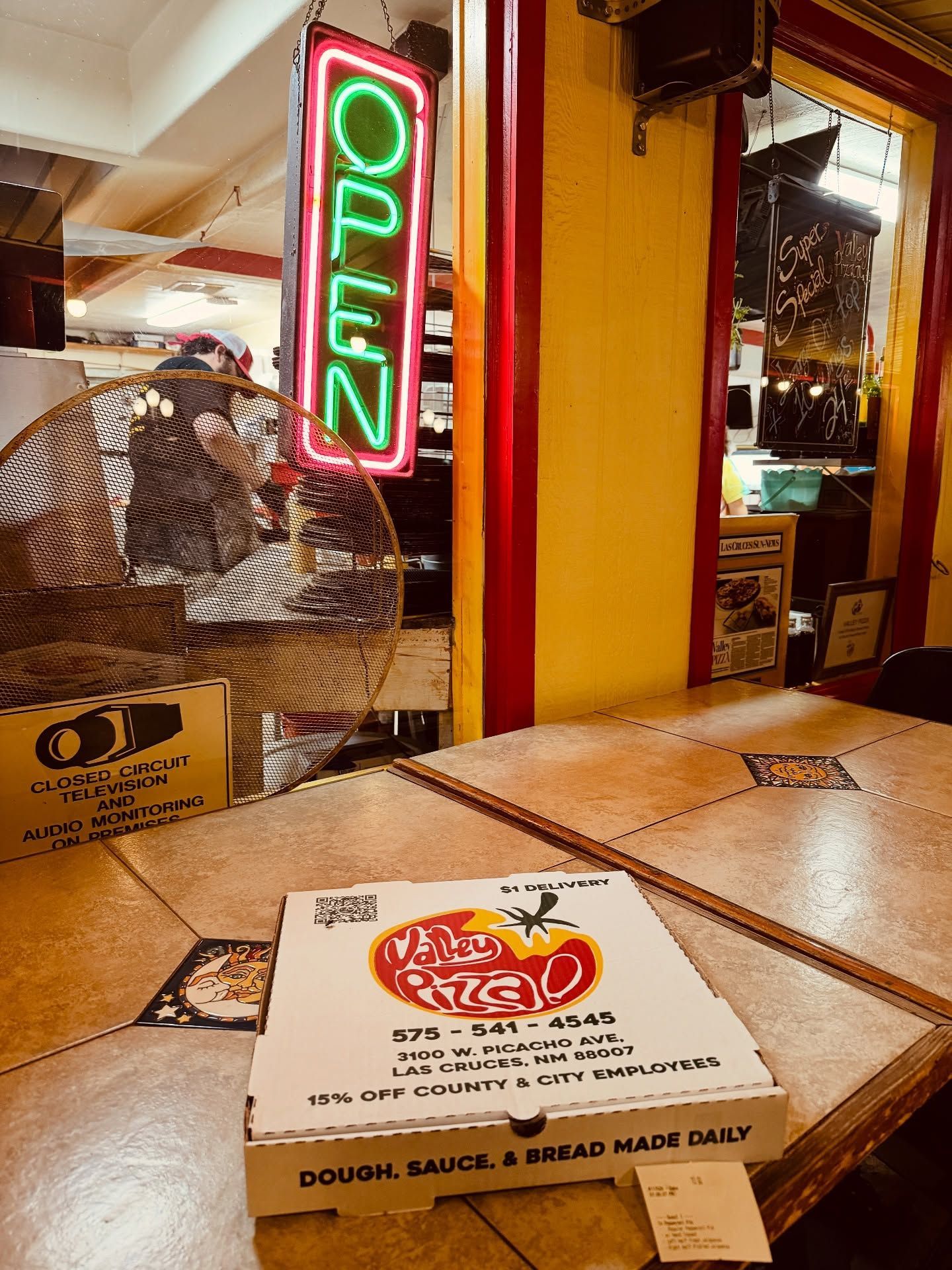 Neon OPEN sign by a restaurant window, with a menu card on a wooden table in warm indoor lighting.